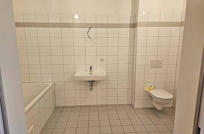Funktionales Badezimmer mit weißen Fliesen, Badewanne, Waschbecken und Wand-WC.