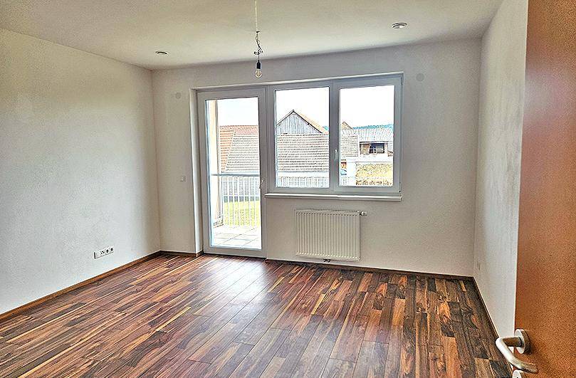Helles Zimmer mit Laminatboden, großem Fenster und direktem Zugang zu einem Balkon.