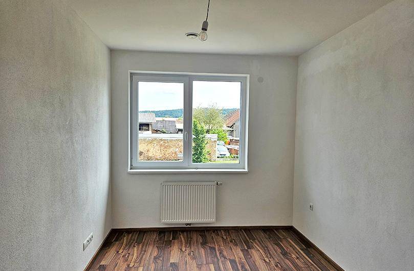 Leeres Zimmer mit Laminatboden, großem Fenster und Blick ins Grüne, ideal als Schlafzimmer.