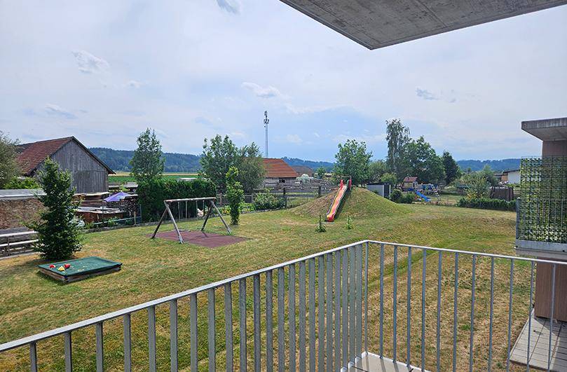 Balkon mit Blick auf einen Gemeinschaftsspielplatz und grüne Umgebung, ideal für Familien.