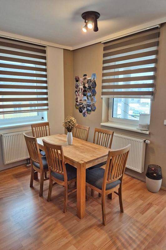 Gemütlicher Essbereich mit Holztisch, Stühlen und zwei Fenstern mit Rollos.