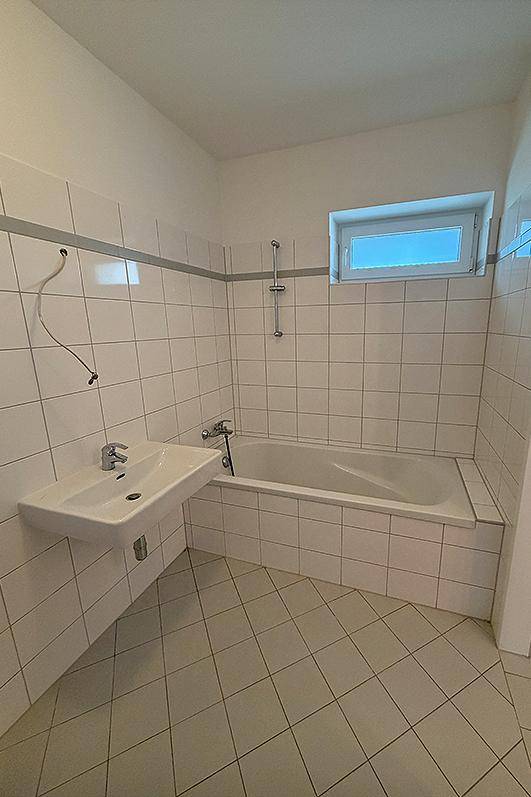 Badezimmer mit Badewanne, Waschbecken und Fenster, komplett gefliest in Weiß.