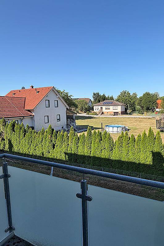 Weitläufiger Blick vom Balkon über grüne Hecken und benachbarte Häuser.