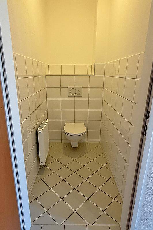 Kleines Gäste-WC mit weiß gefliesten Wänden und Boden sowie einem Heizkörper.