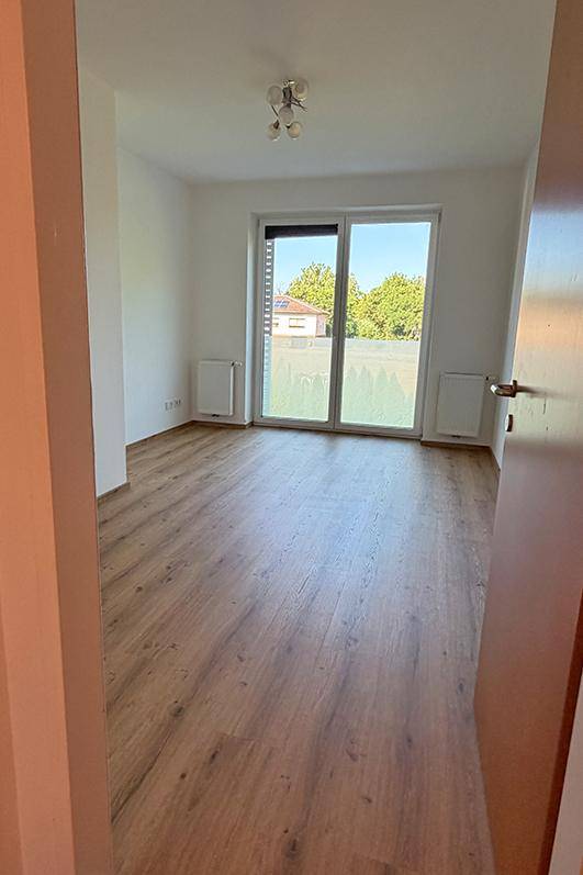 Helles Zimmer mit Laminatboden und großem Fenster, bereit zur individuellen Gestaltung.