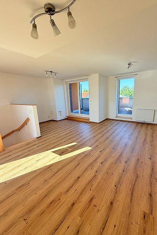 Heller Wohnbereich mit Laminatboden und Zugang zu einem Balkon, gut belichtet.
