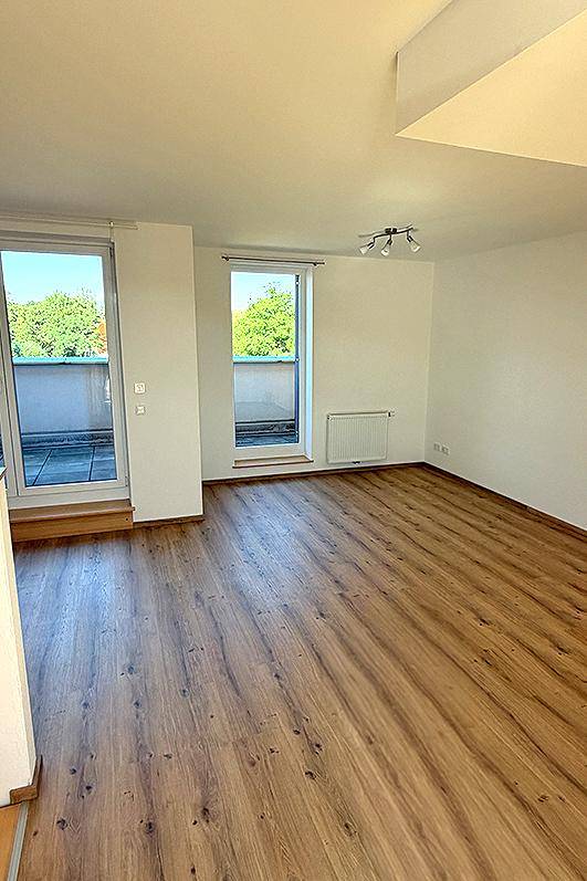 Geräumiger, heller Wohnbereich mit Laminatboden und Zugang zu einem Balkon.