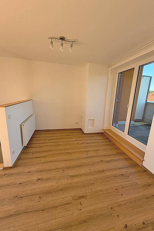 Heller Wohnbereich mit Laminatboden und Zugang zu einem Außenbereich.