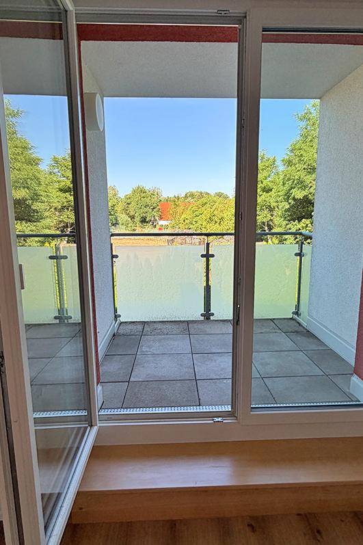 Balkon mit Fliesenboden und Glasbrüstung, bietet einen Blick ins Grüne.