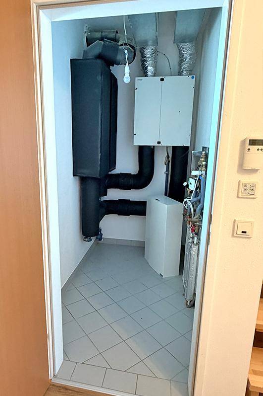 Technikraum mit Lüftungsanlage und Heizungsinstallationen auf gefliestem Boden.