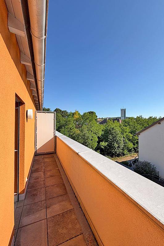 Langer Balkon mit Fliesenboden und oranger Fassade, bietet einen weiten Blick.