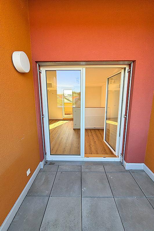 Blick vom Balkon in einen hellen Innenraum mit Laminatboden und viel Tageslicht.