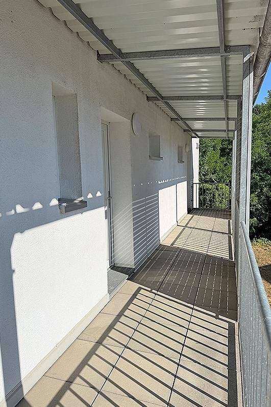 Überdachter Balkon mit Fliesenboden und Blick ins Grüne, bietet Schutz vor Sonne.