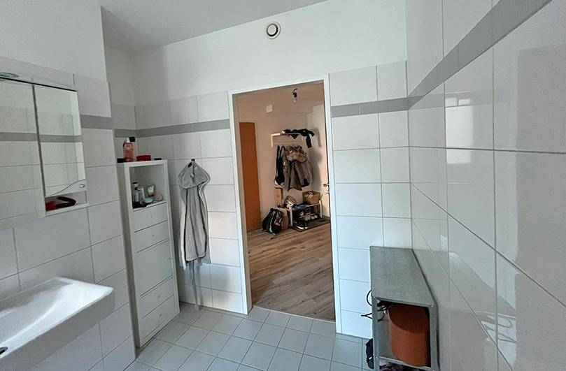 Modern gefliestes Badezimmer mit Waschbecken, Spiegelschrank und Zugang zum Flur.
