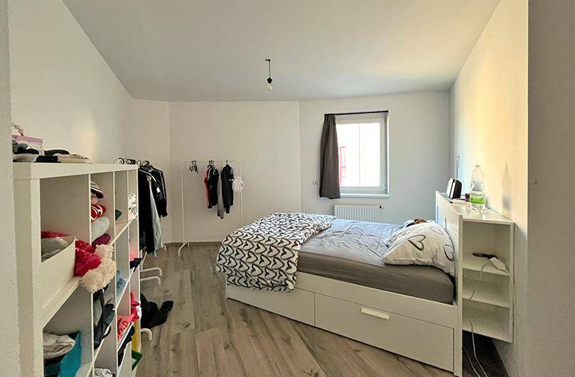 Schlafzimmer mit Bett, praktischen Regalen und einem Fenster, das für ausreichend Helligkeit sorgt.