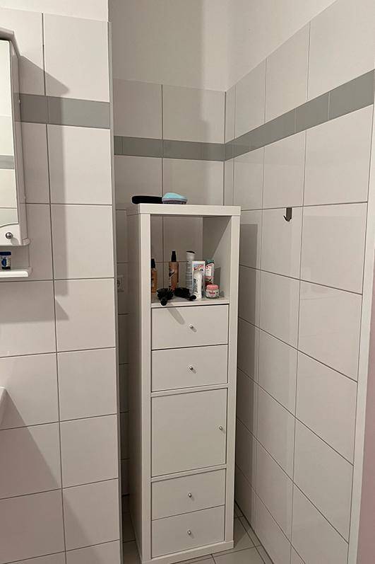 Weißer Hochschrank im Badezimmer bietet praktischen Stauraum für Pflegeprodukte und Handtücher.