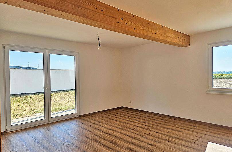 Lichtdurchfluteter Raum mit sichtbaren Holzbalken, Laminatboden und direktem Gartenzugang.
