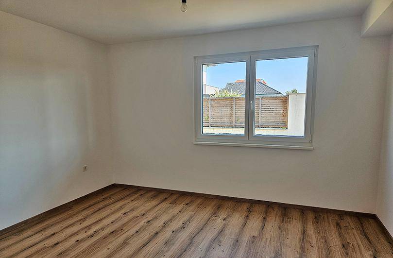 Helles Schlafzimmer mit Laminatboden und Fenster, das einen Blick auf den Garten bietet.