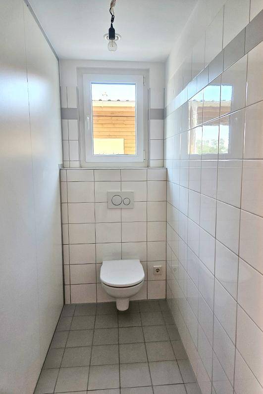 Separates Gäste-WC mit wandhängender Toilette, Fenster und hellen Fliesen.