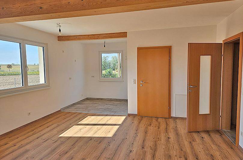 Geräumiger Wohnbereich mit Laminatboden, Holzbalken und Fenstern mit Blick ins Grüne.