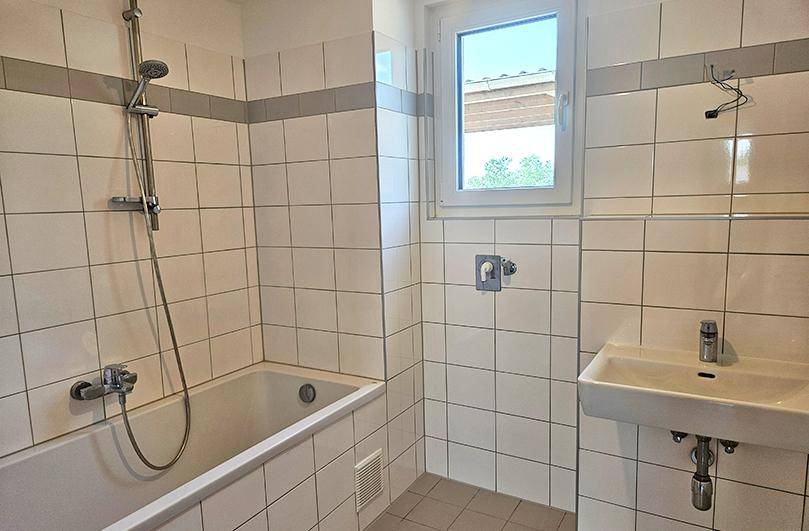 Funktionales Badezimmer mit Badewanne, Duschfunktion, Waschbecken und weißen Wandfliesen.