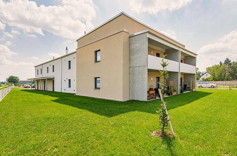 Ansicht des modernen Wohngebäudes mit beiger und weißer Fassade sowie Balkonen und Rasenfläche.