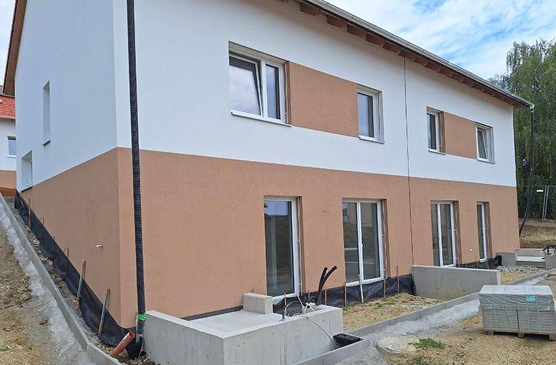 Neubau-Doppelhaushälfte mit zweifarbiger Fassade im Bauzustand und großen Fenstern.