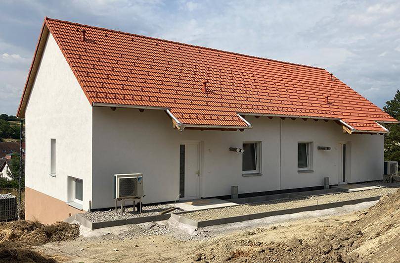 Außenansicht eines Neubaus mit rotem Ziegeldach und weißer Fassade in ländlicher Umgebung.