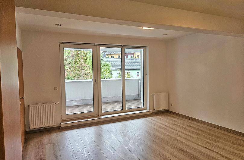 Geräumiges Wohnzimmer mit großen Schiebetüren zum Balkon und Blick auf die Umgebung.