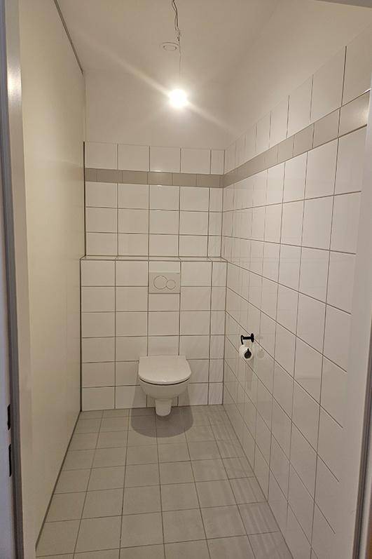 Kleines, hell gefliestes WC mit wandhängender Toilette und schlichtem Design.
