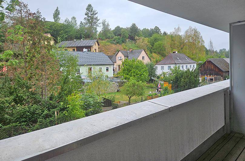 Balkon mit weitem Blick über eine grüne Wohngegend und bewaldete Hügel.