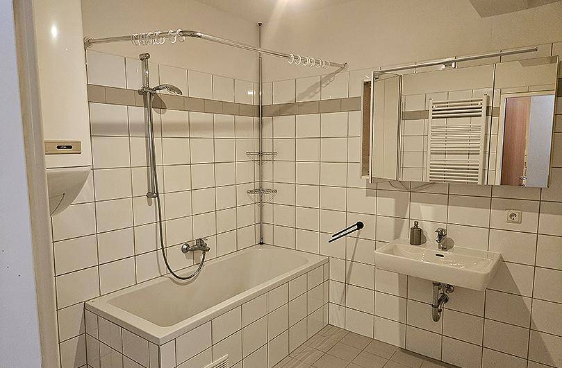 Gefliestes Badezimmer mit Badewanne, Duschvorrichtung, Waschbecken und Spiegelschrank.