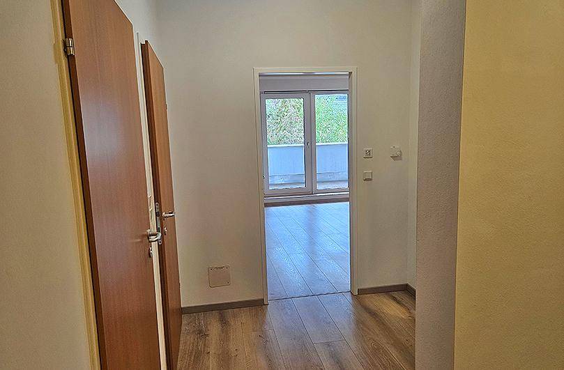 Gangbereich mit Zugang zu einem Raum mit Balkon und Blick ins Grüne.