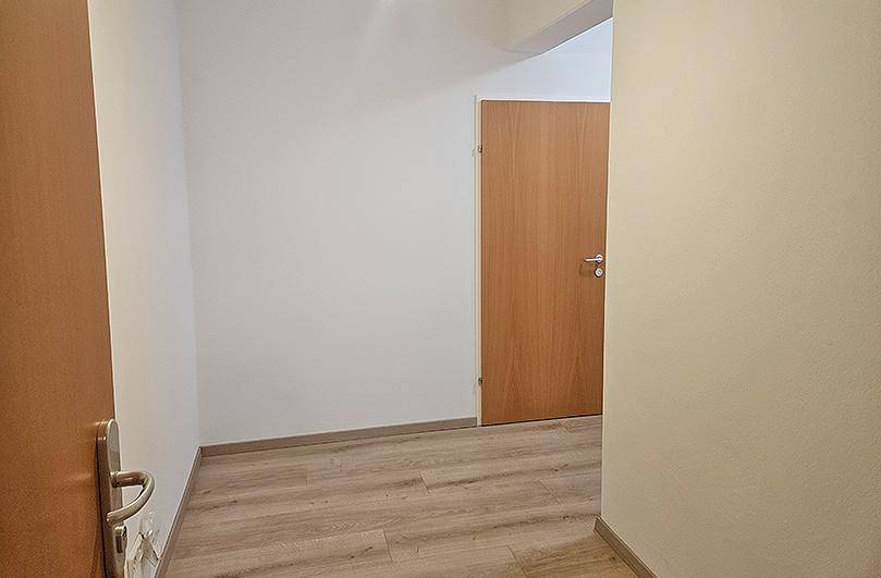 Heller Flur mit Holzbodenoptik und weißen Wänden, der zu weiteren Räumen führt.