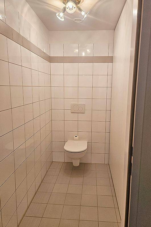 Kleines WC mit weißen Wandfliesen, wandhängender Toilette und grauen Bodenfliesen.