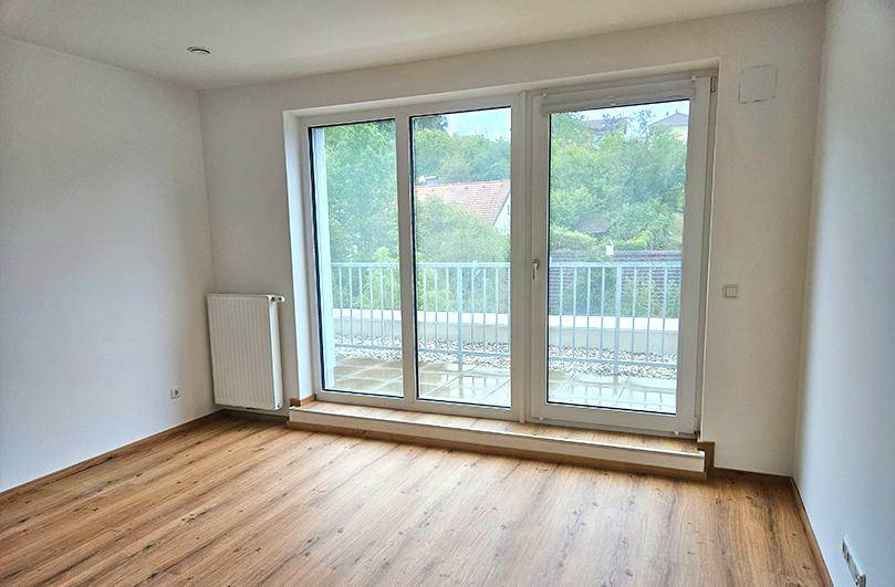 Heller Raum mit Laminatboden und großer Glasfront, die Zugang zu einem Außenbereich bietet.