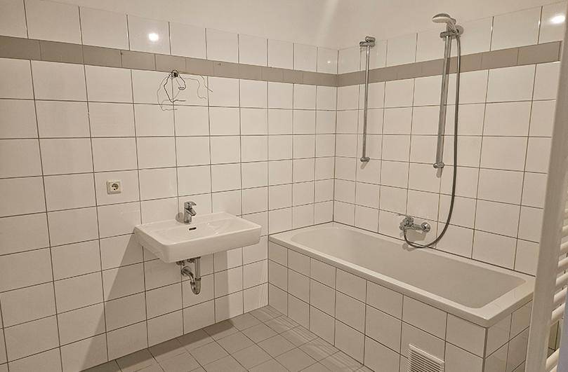 Badezimmer mit weißen Fliesen, Badewanne mit Duschfunktion und einem Waschbecken.
