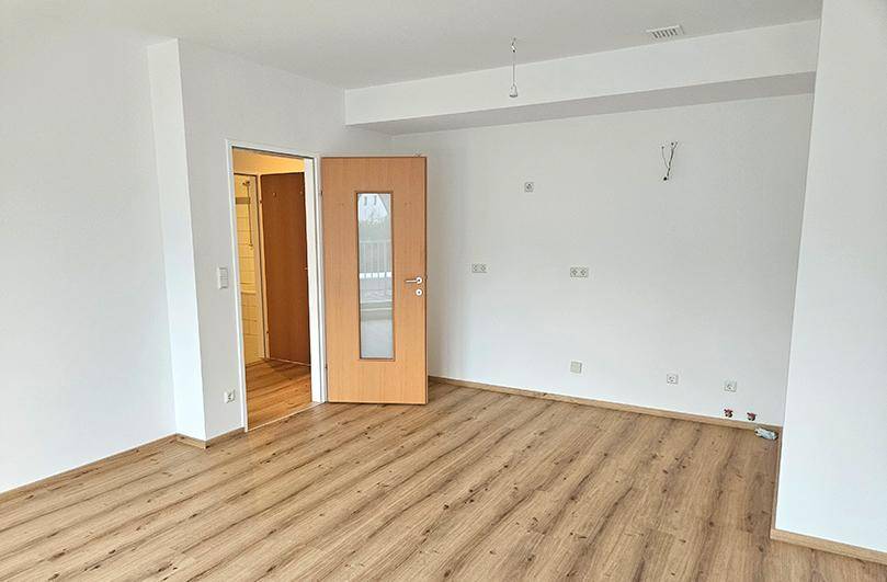 Geräumiges, leeres Wohnzimmer mit Laminatboden und weiß gestrichenen Wänden, bereit zur Einrichtung.
