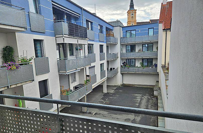 Ansicht eines modernen Wohnkomplexes mit blauen Akzenten, Balkonen und einem Innenhof.