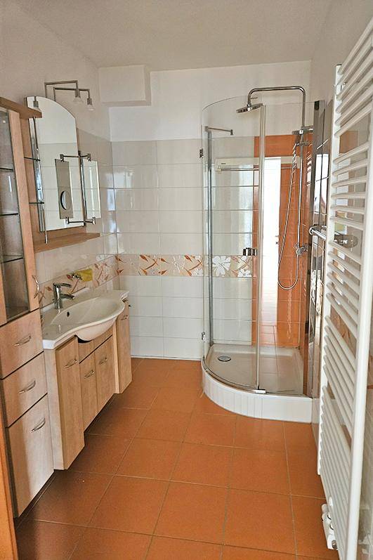 Badezimmer mit orangefarbenen Fliesen, Holzwaschtisch und einer modernen Duschkabine sowie Handtuchheizkörper.
