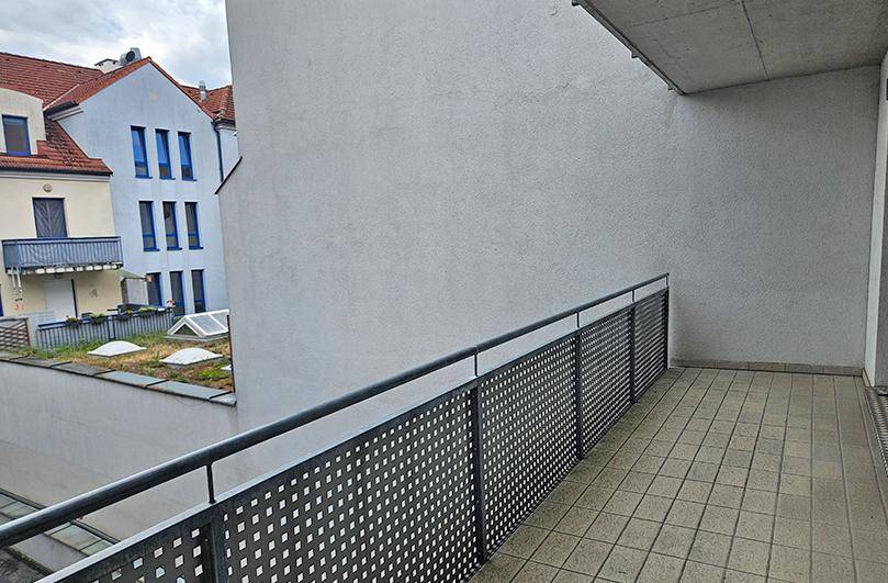 Geräumiger Balkon mit Fliesenboden und Metallgeländer, der einen Blick auf den Innenhof bietet.