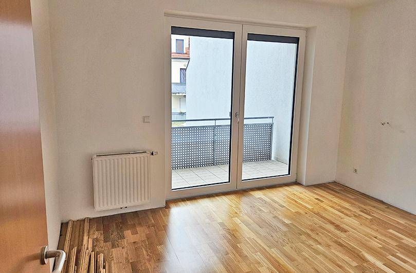 Helles Schlafzimmer mit Parkettboden, weiß gestrichenen Wänden und direktem Zugang zu einem kleinen Balkon.