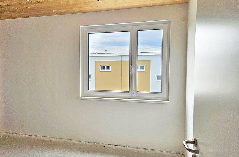 Unmöblierter Raum mit großem Fenster und Blick auf ein gegenüberliegendes Gebäude.