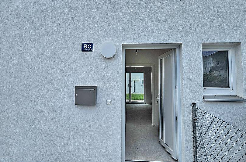 Eingangsbereich eines modernen Gebäudes mit Hausnummer, Briefkasten und Blick ins Innere.