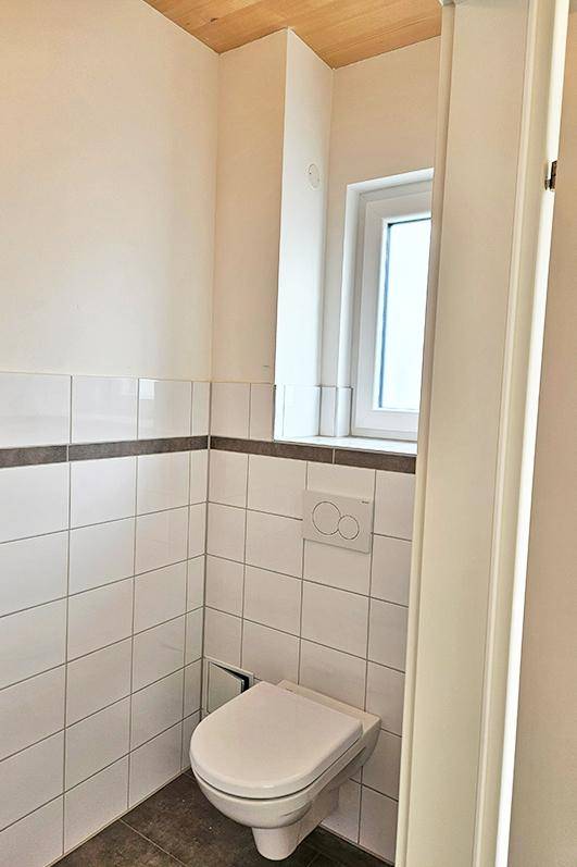 Helles Gäste-WC mit wandhängender Toilette, Fenster und modernen Fliesen.