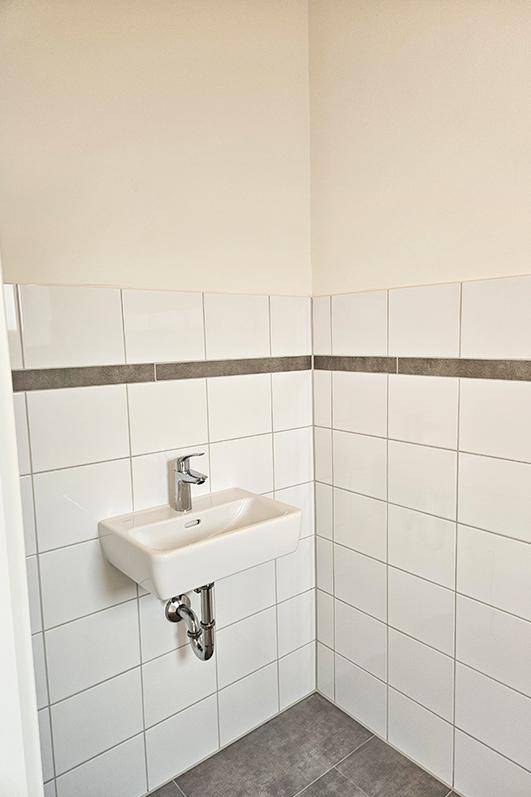 Modern gefliestes Gäste-WC mit Einzelwaschbecken und schlichtem Design.