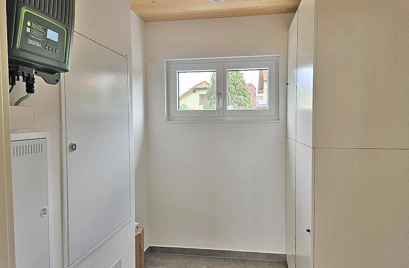 Hauswirtschaftsraum mit Photovoltaik-Wechselrichter, Einbauschränken und Fenster.