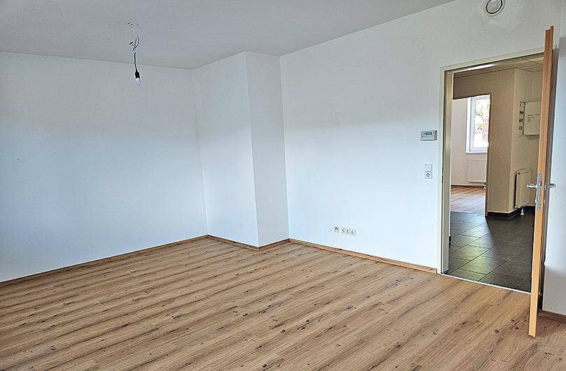 Geräumiges Zimmer mit Laminatboden und Übergang zu einem gefliesten Bereich, ideal für Wohnzwecke.