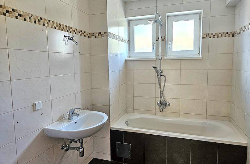 Badezimmer mit Badewanne, Waschbecken und zwei Fenstern für ausreichend Tageslicht.