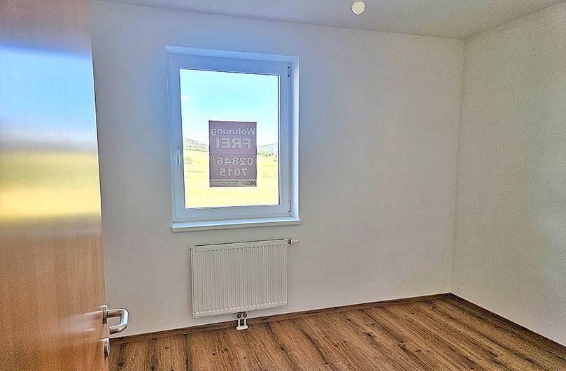 Leeres Zimmer mit Laminatboden und Fenster, das einen weiten Blick in die Landschaft bietet.
